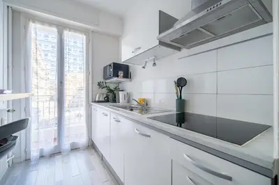 a kitchen with white cabinets and a black counter top at Port de Nice - Studio with balcony in Nice