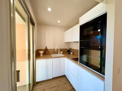 a kitchen with white cabinets and a black appliance at Studio cosy - Vue mer - Terrasse - Parking in Saint-Laurent-du-Var