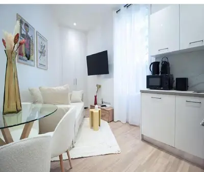 a white living room with a glass table and a kitchen at Nid Douillet au Cœur de Nice avec terrasse et clim in Nice