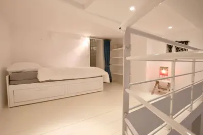 a white bedroom with a bed and a staircase at Charmant appartement au sein de la vieille ville in Villefranche-sur-Mer