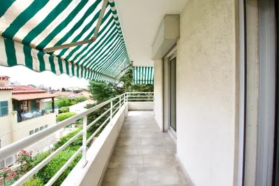 a balcony with a green and white umbrella at Terrasse, piscine & parking sur la Côte d'Azur in Saint-Laurent-du-Var