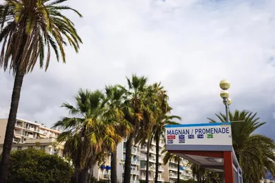 a sign in front of palm trees and a building at Cosy Nice Promenade des Anglais Beach Apartment 2 rooms in Nice
