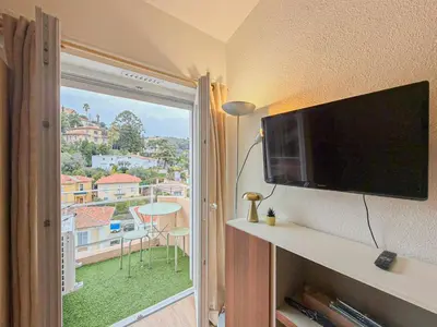 a living room with a flat screen tv and a balcony at Proche mer - 2 pers, AC in Nice