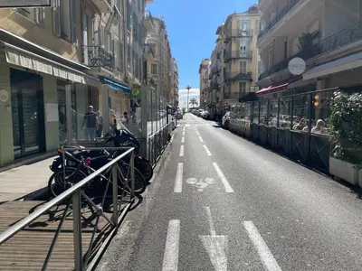 an empty street in a city with people sitting outside at One-Bedroom Apartment near Promenade des Anglais in Nice