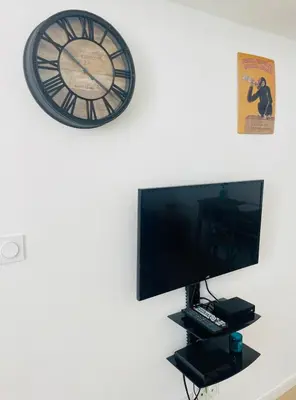 a clock on a wall above a computer monitor and a tv at Bright modern studio, Nice Port, walk to tram and beach! in Nice