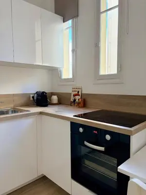 a kitchen with white cabinets and a black stove top oven at Studio avec balcon - Centre-ville & plage à 2 min in Nice