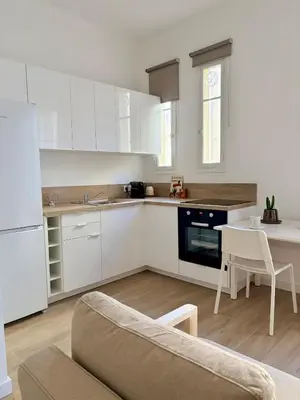 a kitchen with white cabinets and a table and a couch at Studio avec balcon - Centre-ville & plage à 2 min in Nice