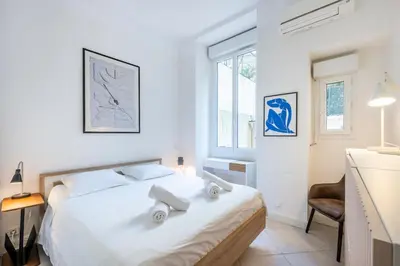 a white bedroom with a bed and a chair at The Apartment with the Garden Studio in Nice