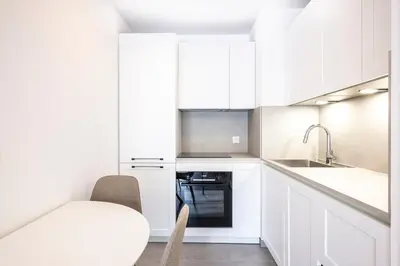 a white kitchen with white cabinets and a sink at Appartement du Port with park view in Nice