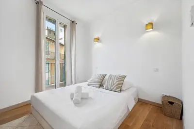 a white bedroom with a bed and a window at L'Essentiel Confort - Solaire, Plage, Vieux Nice - by Studio Y in Nice