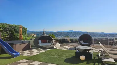 a patio with two chairs and a playground at Penthouse - Vue mer panoramique - SPA privé - Piscine commune in Saint-Laurent-du-Var