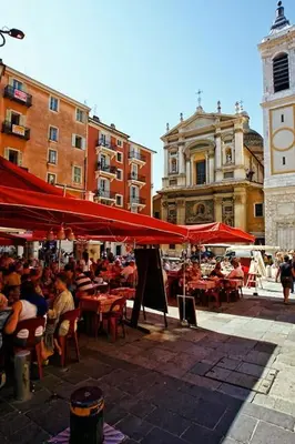 a group of people sitting at tables under red umbrellas at Place Rossetti - Charming Apartment in Nice