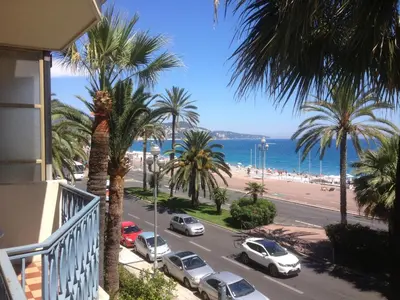 a balcony view of a street with palm trees and a beach at Le Grand Sud in Nice
