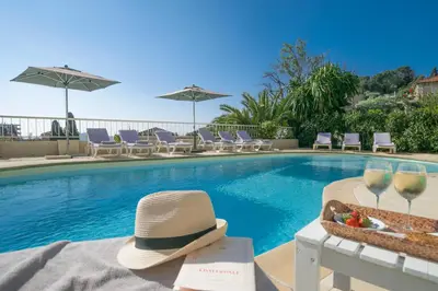 a hat and wine glasses next to a swimming pool at Hôtel La Fiancée du Pirate in Villefranche-sur-Mer