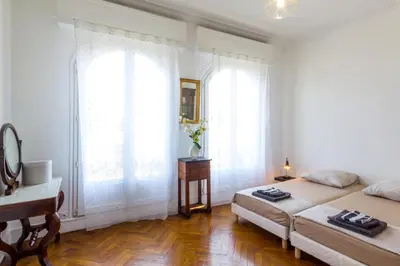 a bedroom with two beds and a desk and two windows at Beautiful apartment by the sea front in Nice