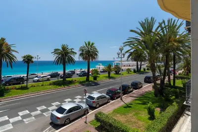 a street with parked cars and palm trees and the ocean at Beautiful apartment by the sea front in Nice
