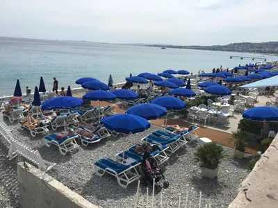 a beach with blue umbrellas and chairs and the ocean at Olma in Nice