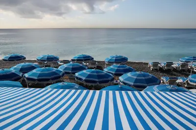 a group of blue umbrellas and chairs on a beach at Chambre chez l'habitant Nice Baie des Anges in Nice