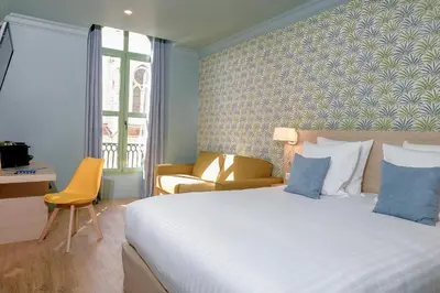a bedroom with a large bed and a yellow chair at Hôtel Du Centre, un hôtel AMMI in Nice