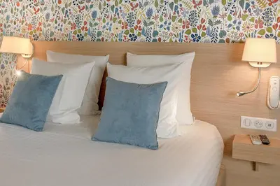 a bed with white pillows and blue pillows at Hôtel Du Centre, un hôtel AMMI in Nice