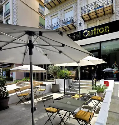 a group of tables and chairs with an umbrella at Hotel Carlton Nice in Nice