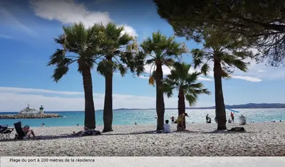 people on a beach with palm trees and the ocean at Residence Heliotel Marine - maeva Home in Saint-Laurent-du-Var