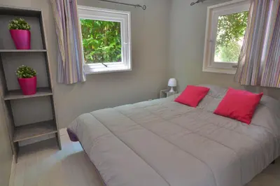 a bedroom with a bed with red pillows and two windows at Camping Les Cent Chênes in Saint-Jeannet