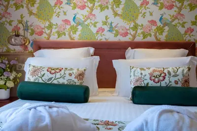 a bed with two pillows and a floral wallpaper at Hôtel Petit Palais in Nice
