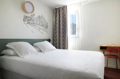 a bedroom with a bed with white sheets and a window at Hotel Restaurant Isidore by Soniho in Nice