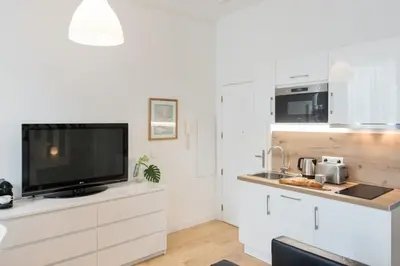 a kitchen with white cabinets and a flat screen tv at Le Studio Graphite Welkeys in Nice
