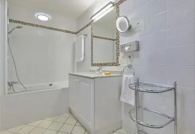 a white bathroom with a sink and a tub and a mirror at La Résidence de La Réserve in Beaulieu-sur-Mer