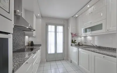 a white kitchen with white cabinets and a window at La Résidence de La Réserve in Beaulieu-sur-Mer