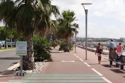 people walking on a sidewalk near a beach with palm trees at Maresol in Cagnes-sur-Mer