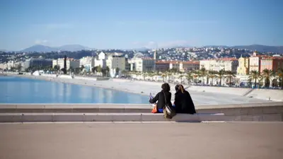 two women sitting on a wall looking at the beach at 