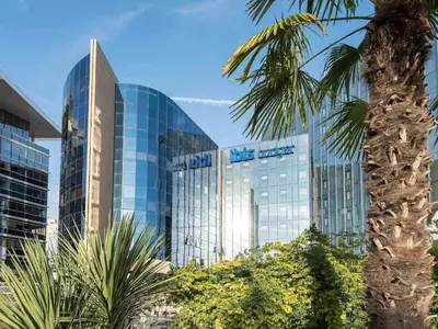 a tall glass building with a palm tree in front of it at ibis budget Nice Aeroport in Nice