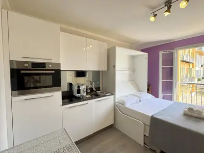 a small kitchen with white cabinets and a bed at ApartHotel Riviera Nice Côte d'Azur - Old Town - Studio AC - Sea View - 50m Promenade des Anglais- LA MAISON LINDA in Nice