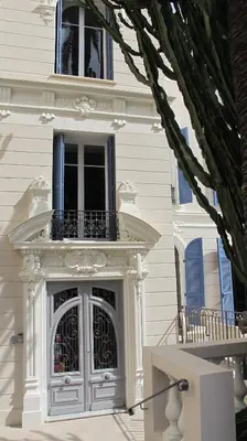 a white house with a balcony and a door at Hotel Le Havre Bleu in Beaulieu-sur-Mer