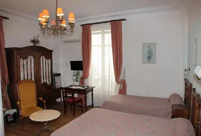a bedroom with two beds and a desk and a table at Hotel Cronstadt in Nice