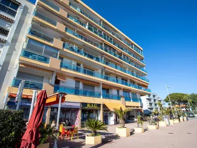 a beach with palm trees and buildings in the background at Apartment La Pinède-1 by Interhome in Cagnes-sur-Mer