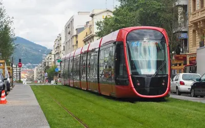a red tram on a city street with people standing next to it at Luxe et charme Méditerranéen face à la promenade des Anglais in Nice