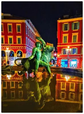 a statue in the middle of a city at night at Le Petit Trianon et le Charme des Suites in Nice