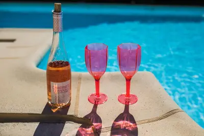a bottle of wine and two wine glasses next to a swimming pool at LA CASETTA DEI FIORI VI3078 in Nice