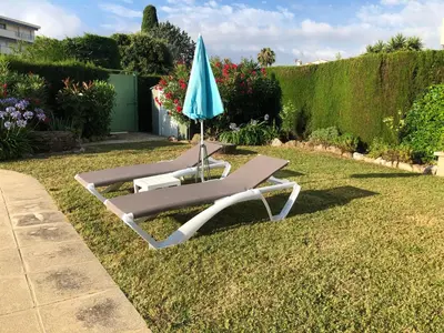 a lounge chair with an umbrella on the grass at Villa C3 Arthur Rimbaub chambre d’hôte piscine proche mer plage 600m in Cagnes-sur-Mer