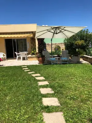 a patio with two chairs and an umbrella on a lawn at Villa C3 Arthur Rimbaub chambre d’hôte piscine proche mer plage 600m in Cagnes-sur-Mer