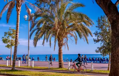 a person riding a bike on a sidewalk next to the beach at Palais Massena - Easy Home Booking in Nice