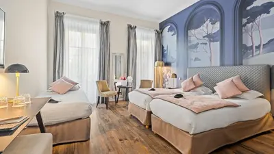 a hotel room with two beds and a desk at Hotel Villa Victoria in Nice
