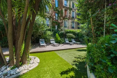 a garden with chairs and trees and a building at Hotel Villa Victoria in Nice