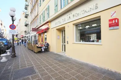 a street with people sitting outside of a store at Hôtel de la Fontaine in Nice