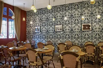 a restaurant with tables and chairs in a room with wallpaper at Hotel Le Grimaldi by Happyculture in Nice