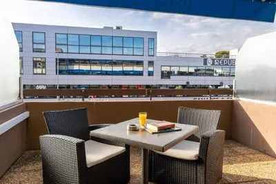 a table and chairs on a balcony with a building at The Originals City, Hôtel Galaxie, Nice Aéroport in Saint-Laurent-du-Var